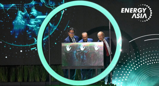Prime Minister Anwar Ibrahim with Tan Sri Tengku Muhammad Taufik and Dr. Daniel Yergin launch Energy Asia 2025 by placing hands on an illuminated panel inside a glowing circle, with a digital globe in the background.