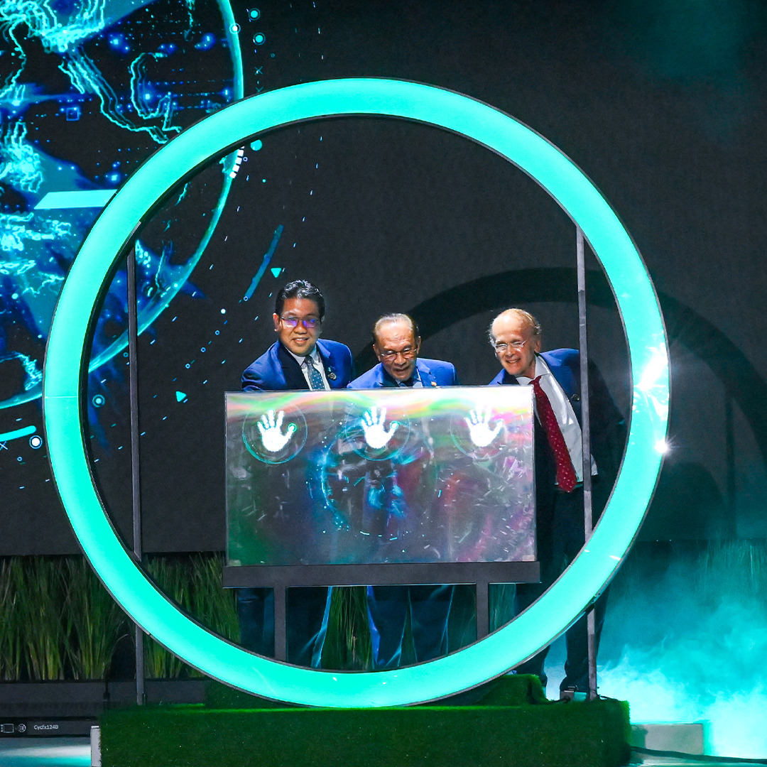 Prime Minister Anwar Ibrahim with Tan Sri Tengku Muhammad Taufik and Dr. Daniel Yergin launch Energy Asia 2025 by placing hands on an illuminated panel inside a glowing circle, with a digital globe in the background.